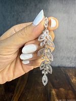 Photo shows front view of the sterling silver articulated leaf pendant held by hand, highlighting the clear stones and leaf design details.