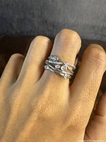 Rings photographed on finger showing cross-over layered design with clear stones.