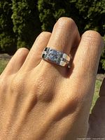 Contemporary sterling silver gentlemans ring worn on finger, showing clear central stone and side stones.