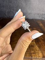 Sterling silver ring held between fingers showing details of the central clear stone, halo design, and band stones.