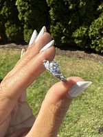 Ring held between thumb and forefinger, showing clear/blue round stone and engraved sterling silver band