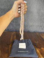 Full view of the necklace held above the Imperial branded pouch with care booklet on a wooden surface.