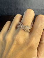 Ring worn on finger, showing its cross-over style with clear stones and rose-gold overlay.