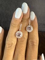 Front view of earrings held by hand showing central pink stone and halo of clear stones.