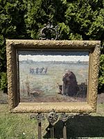 Full front view of framed oil painting outdoors on metal stand, showing entire artwork and frame