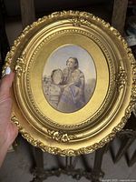 Miniature watercolour painting of a seated woman holding a tambourine, in an ornate carved gold oval frame, photographed outdoors showing a hand holding the frame to illustrate scale.