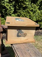 Front and side view of wooden box showing carved and painted bird motif on the side and abalone insets on the corners of the lid.