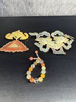 Group of three embroidered antique Asian dress garment appliqués in various colors with a colorful beaded bracelet in front on a black background.