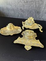 Three solid brass inkwells displayed on black surface