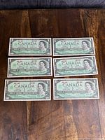 Front side of all six uncirculated Canadian $1 bills laid out on wood surface.