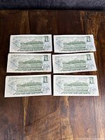 Six Canadian $1 bank notes showing the back side with green scenic design.