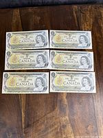 Front faces of the six Canadian $1 bank notes, laid in two rows of three, showing Queen Elizabeth II portrait, the text 'Bank of Canada' and value markings.