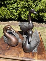 Three bronze duck sculptures arranged on wooden table outdoors showing entire lot