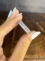 The sterling silver ring held between fingers showing the emerald-cut clear stones around band.