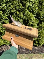 Side view of the cedar box held in hand, showing the carved wolf head mounted on the lid with a feather and copper accent on the front.