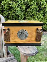 Front view of wooden box showing side animal head carvings, metal plaque and black painted trim