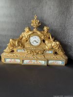 Full front view of the mantle clock showing bronze figures, clock face, porcelain panels and finial on black background