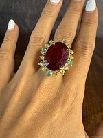 Front view showing large oval natural ruby with alternating green and yellow stones surrounding it, worn on hand.