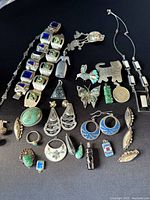 Top-down view of assorted vintage Mexican jewelry items including bracelets, rings, pendants, earrings, and pins arranged on a black surface.