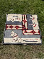 Full view of the large early antique Inuit hand embroidered textile laid flat outdoors on grass, showing the full square shape and detailed embroidery design.