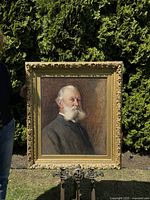 Full view of framed portrait leaning on an easel outdoors with greenery behind