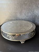 Full view of the large vintage silver-plated cake stand showing engraved top surface and decorative feet