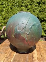 Front view of raku vase showing green matte glaze with raised drip decoration in brown and red tones.