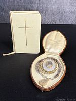Overview of ivory miniature bible with gilt cross and open leather jewelry box containing bracelet and brooch