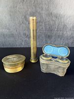 Group of three military interest items: brass telescope, brass artillery shell trench art container, and a pair of binoculars in fabric leather case.