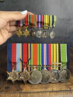 Overall view of full-size and miniature medal sets displayed together on table and held by hand.