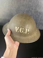 Full view of olive green war era helmet with 'V.C.P.' painted in white stencil on front.