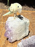 Close-up of carved bird figurine perched on light purple amethyst geode base