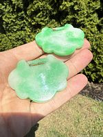 Two carved jade pendants shaped like stylized clouds shown resting on a palm with visible green and white coloring and metal loops.