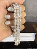 Close-up of bracelet held in hand over black and white jewelry box, showing filigree panels and stone settings