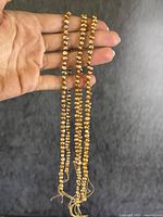 Two strands of irregularly shaped and variously sized chocolate pearls being held by hand against a neutral background, showing overall length and arrangement of strands.