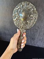 Full view of the antique sterling silver handheld vanity mirror showing cherub and putti motifs on the back.