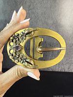 Close-up front view of the antique gold-filled oval belt buckle showing floral design and purple stones.