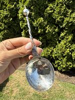 Antique sterling silver ladle held outdoors showing twisted handle and the ladle bowl with wear and tarnish.