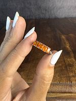 Close-up of the sterling silver ring showing five vivid orange stones set along the band held between fingers.