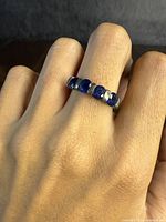 Ring worn on finger showing front detail with five alternating blue stones set in sterling silver band.