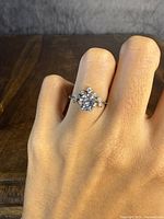 Ring on finger showing large central clear stone and floral halo of smaller stones.