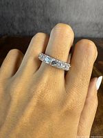 Ring worn on finger showing front view of half eternity band with clear stones in sterling silver.