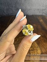 Close-up of the ring held between fingers showcasing the large yellow round stone and one clear triangular side stone.