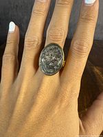 Close-up photo of the carved abalone cameo on a silver and gold overlay ring on hand, showing side profile of the cameo.