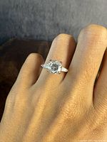 Ring on finger showing clear round central stone with baguette side stones in a sterling silver setting