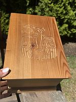 Top view showing carved raven and moon design on cedar box lid under sunlight with fine wood grain visible.