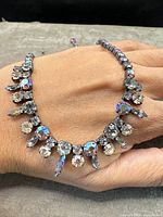 Necklace displayed across hand showing full front view of clustered round and marquise-cut rhinestones.