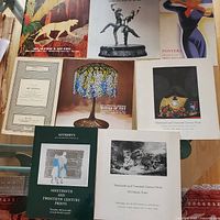 Photo showing multiple Sotheby's auction catalogs and posters with Art Nouveau theme, featuring decorative lamps, sculptures, and collectible prints.