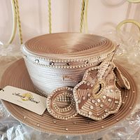 Close-up of derby hat showing layered ribbon, pearl bead and rhinestone floral decoration and Anna Rossi by Moshita Couture tag.