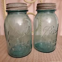Front view of two antique Ball Perfect Mason jars with metal screw tops on fabric surface